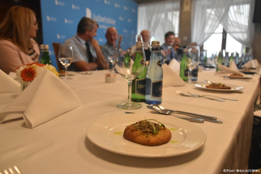 Śniadanie prasowe Europejskiego Festiwalu Smaku. Na pierwszym planie na talerzu znajduje się cebularz, w tle przy stole siedzą uczestnicy konferencji.