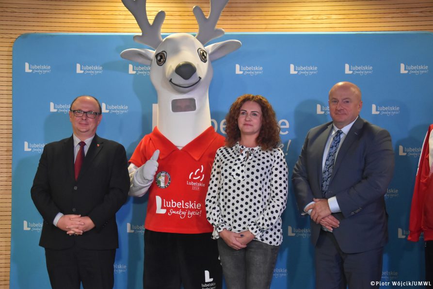 grupowe zdjęcie uczestików konferencji prasowej. Od lewej burmistrz Krasnika Wojciech Wilk, maskotka olimpiady, wiceprezes Lubelskiej Unii Sportu Magdalena Iwaszczuk, marszałek województwa Lubelskiego Jarosław Stawiarski.