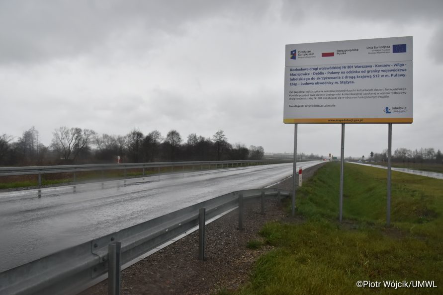 Widok na nową drogę i tablicę informującą o nazwie projektu współfinansowanego z Funduszy Europejskich