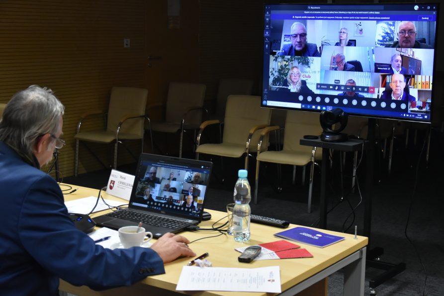 Przy biurku siedzi przewodniczący Stałego Zespołu Roboczego ds. Polityki Społecznej i Ochrony Zdrowia Wojewódzkiej Rady Dialogu Społecznego. W tle, na ekranie wyświetlają się inni członkowie posiedzenia.