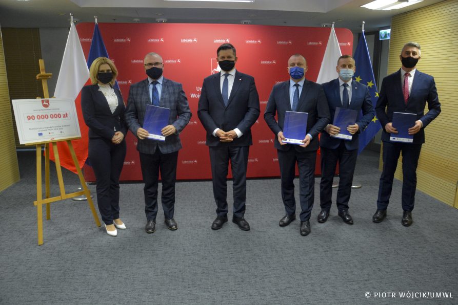 Na zdjęciu 6 osób (wójtowie trzymają teczki z umowami). Po środku stoi członek zarządu województwa Zdzisław Szwed