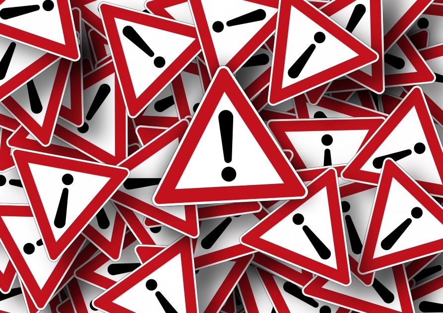 grafika przedstawia znaki informacyjne w postaci trójkątów z czerwoną ramką i białym wypełnieniem, na których widnieje symbol wykrzyknika