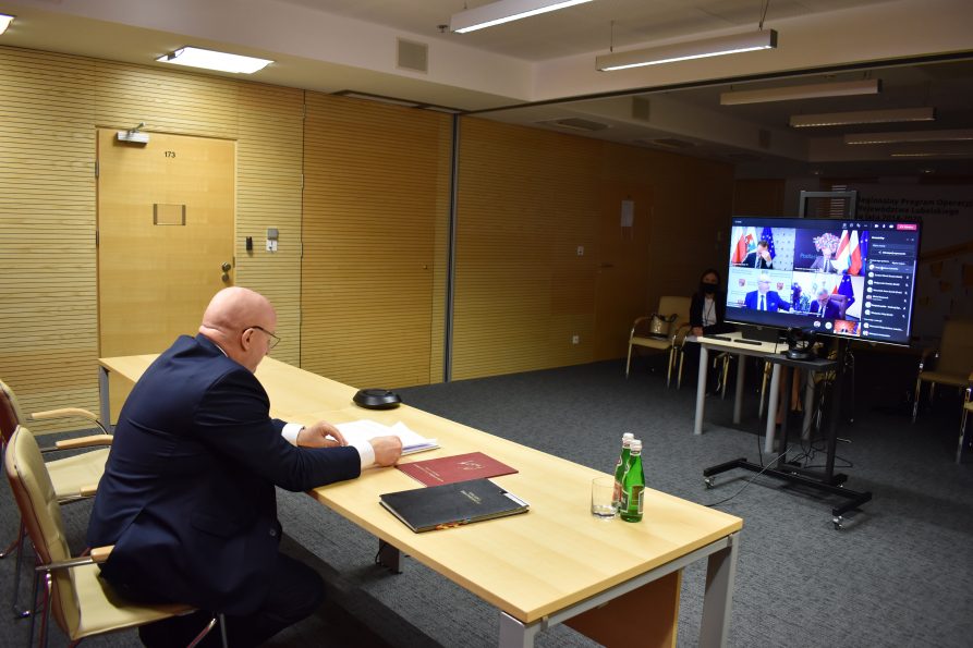 Po lewej przy stole siedzi marszałek Stawiarski, z prawej w tle, telewizor wyświetlający innych członków spotkania.