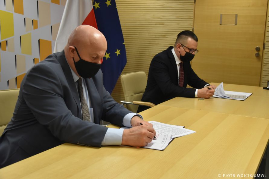 Przy stole siedzą od lewej marszałek Jarosław Stawiarski i prezydent Zamościa Andrzej Wnuk. Podpisują umowy na dofinansowanie.