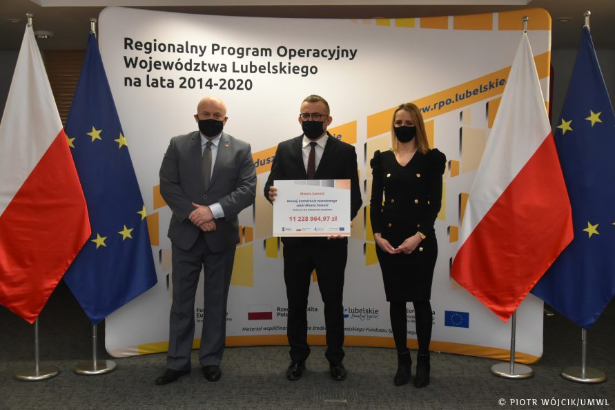 Na tle ścianki Regionalnego Programu Operacyjnego Województwa Lubelskiego i flag Polski i Unii Europejskiej stoją od lewej: marszałek Jarosław Stawiarski, prezydent Zamościa Andrzej Wnuk, skarbnik miasta Zamość Katarzyna Bucior.
