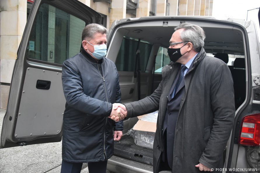 Przy otwartym bagażniku samochodu typu VAN podają sobie dłonie (od lewej) Konsul Generalny Ukrainy w Lublinie Vasyl Pavluk i wicemarszałek Zbigniew Wojciechowski. W środku samochodu widać pudełka ze sprzętem medycznym. W tle fragment ściany frontowej urzędu.