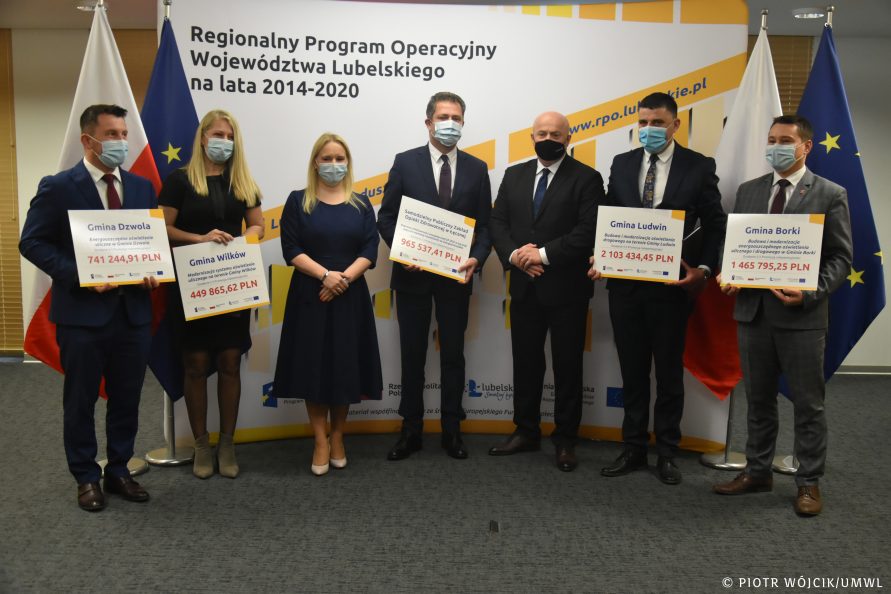 Zdjęcie grupowe beneficjentów i marszałka wojewóztwa. Beneficjenci trzymają symboliczne czeki z wypisanymi kwotami wsparcia