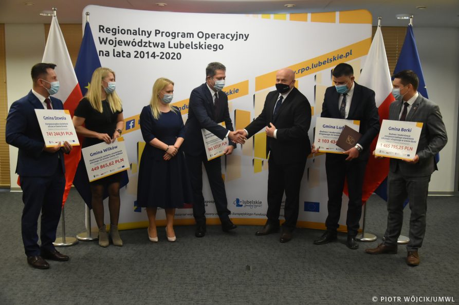 Zdjęcie grupowe beneficjentów i marszałka wojewóztwa. Beneficjenci trzymają symboliczne czeki z wypisanymi kwotami wsparcia