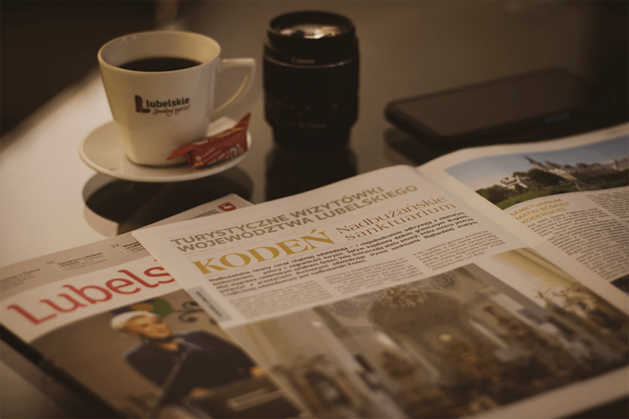na zdjeciu otworzony magazyn Lubelskie.pl, pod nim widać okładkę danego numeru, nad nimi na szklanym stole stoi filiżanka kawy, obiektyw i telefon
