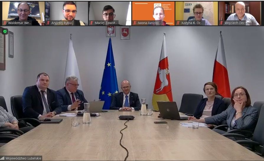 zdjęcie pięciu osób siedzących za stołem na tle trzech flag: RP, UE i Województwa Lubelskiego