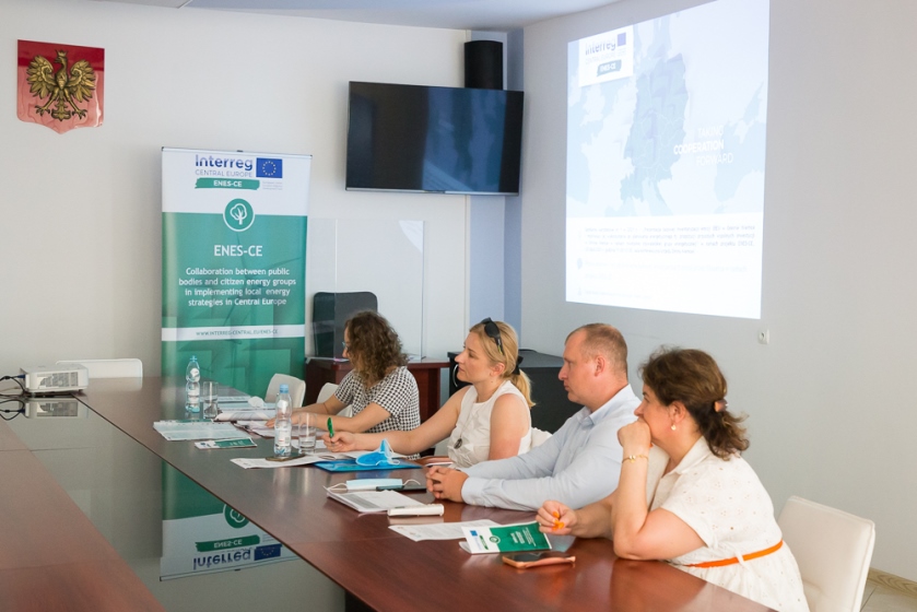 uczestnicy warsztatu przy stole obok roll-up projektu