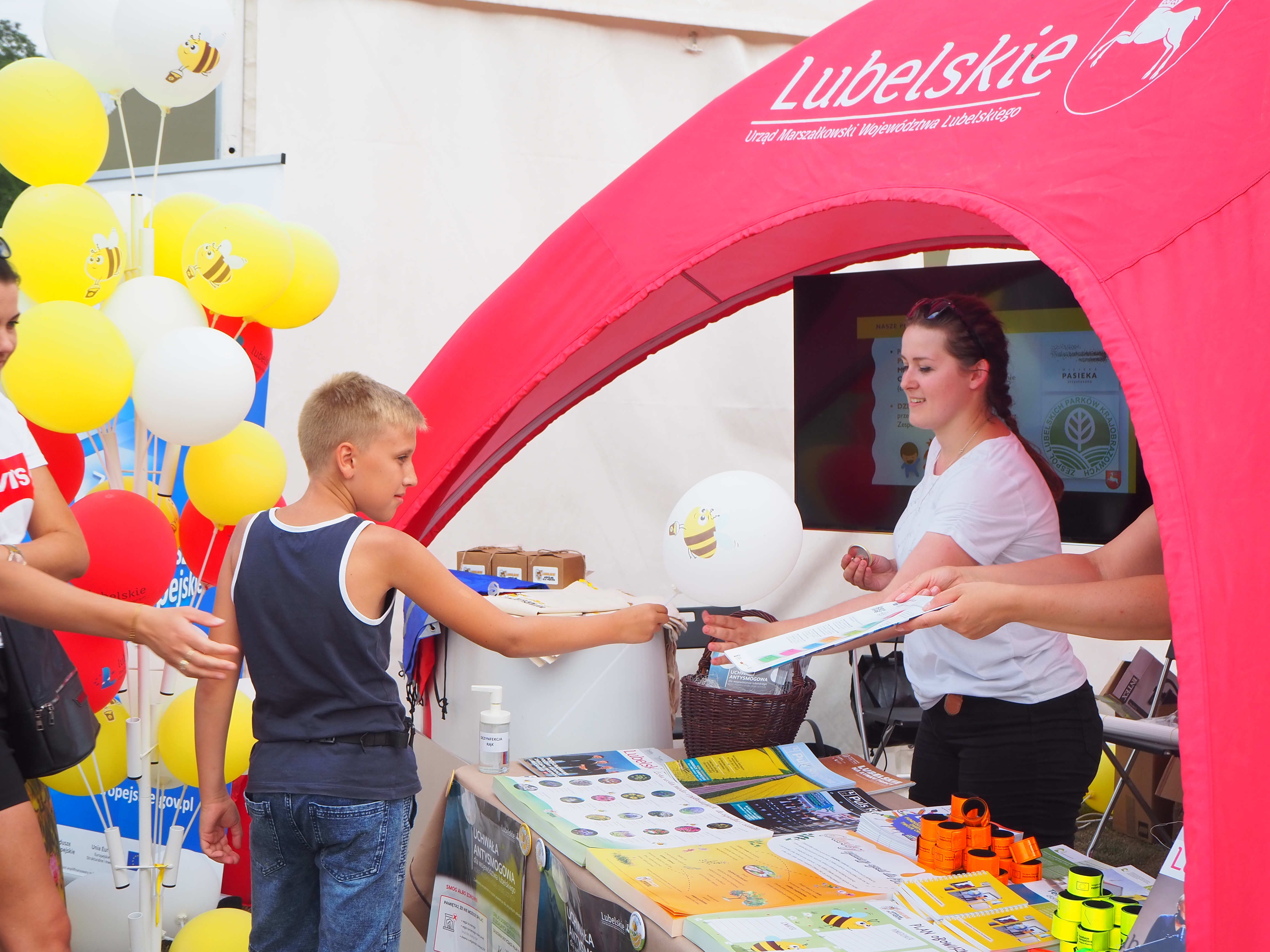 Kobieta (z prawej strony) podaje balonik chłopcu.