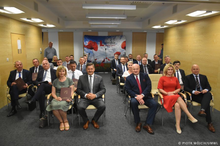 Grupowe zdjecie beneficjentów programu. uczestnicy wydarzenia siedzą na krzesłach na sali konferencyjnej.