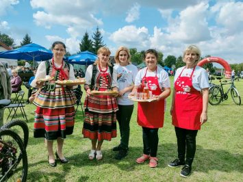 Cztery Panie z Kół Gospodyń Wiejskich prezentujące na tacach swoje dania. Dwie od lewej ubrane w strój ludowy, dwie następne w czerwonych fartuchach kuchennych