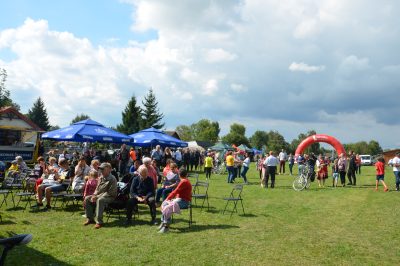 Uczestnicy wydarzenia Komisja konkursowa siedząca przy stole nakrytym białym obrusem, Panie z Koła Gospodyń wiejskich ubrane w stroje ludowe prezentują dania konkursowe
