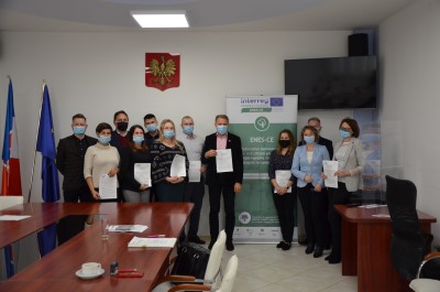 Grupa kobiet i mężczyzn stojących pod ścianą w pokoju. Wszyscy trzymają w rękach dyplomy.