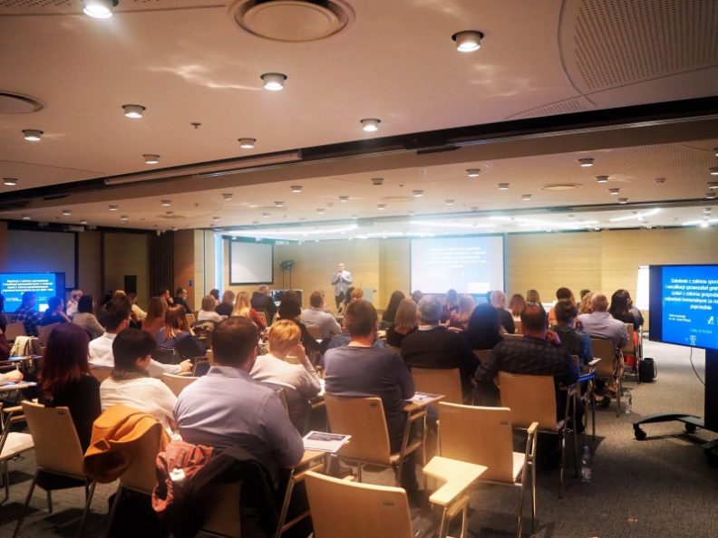 Zdjęcie przedstawiające grupę ludzi siedzących na krzesłach w sali konferencyjnej podczas szkolenia