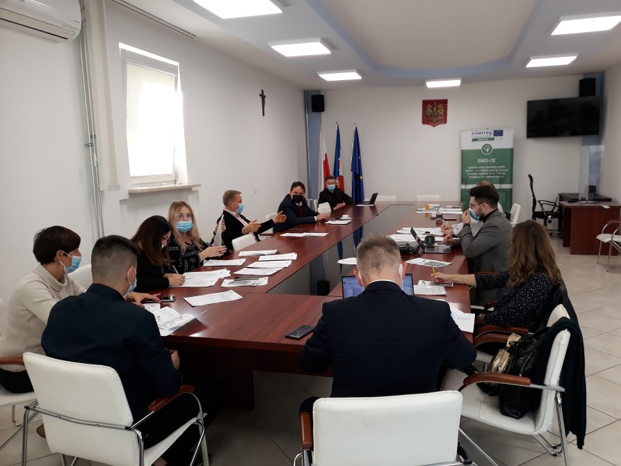 Zdjęcie ukazujące grupe ludzi, kobiet i mężczyzn siedzących w pokoju przy podłużnym stole.