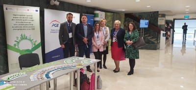 Zdjęcie przedstawiające 6 osób stojących w holu budynku w tym 4 osoby realizujące projekt Doradztwa Energetycznego w Urzędzie Marszałkowskim Województwa Lubelskiego. Z tyłu znajdują się banery projektu doradztwa energetycznego oraz PGE. Z przodu na stolikach są ułożone banery reklamowe projektu doradztwa. Przy stoliku jest ustawione krzesło w kolorze niebieskim.