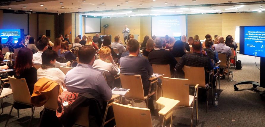 Zdjęcie przedstawiające grupę ludzi siedzących na krzesłach w sali konferencyjnej podczas szkolenia