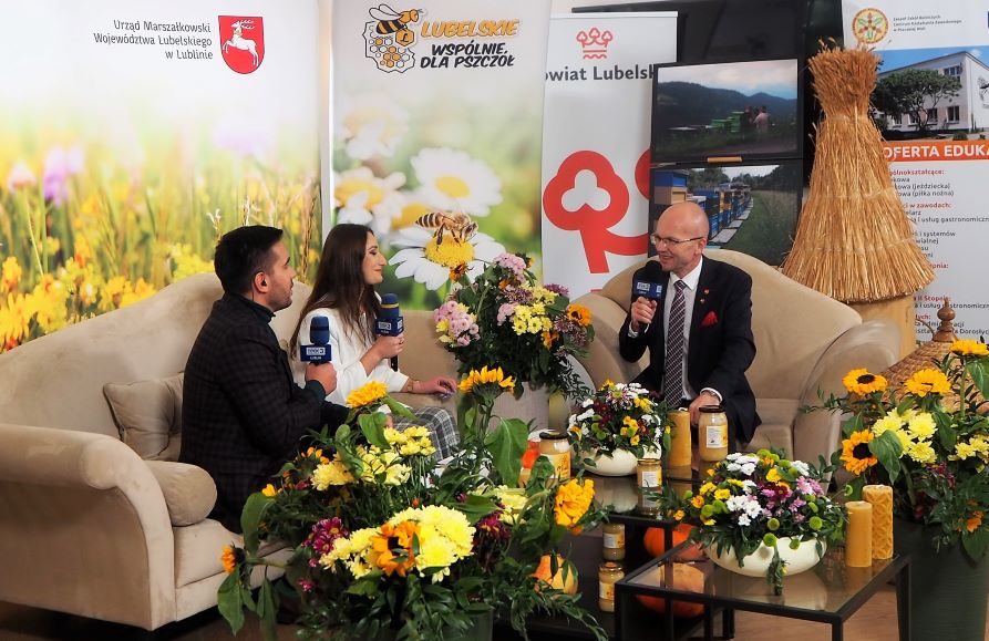 Zdjęcie przedstawia studio TVP w Bystrzycy Nowej. Na kanapach siedzą rozmówcy - dwójka dziennikarzy i gość, Członek Zarządu Województwa Lubelskiego. Za nimi stoją rollupy i ścianki tematycznie nawiązujące do pszczół, kampanii i organizatorów akcji