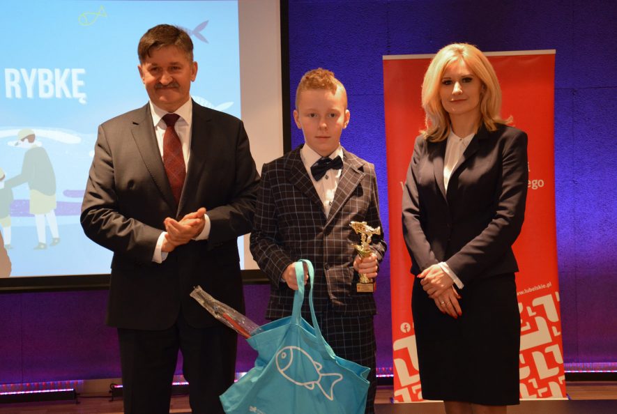 Członek Zarządu Województwa Lubelskiego, Pan Zdzisław Szwed, laureat konkursu „Złap rybkę” oraz Dyrektor Departamentu Rolnictwa i Rozwoju Obszarów Wiejskich, Pani Ewa Szałachwiej. Chłopiec trzyma w ręku pamiątkowy puchar oraz niebieską torbę z rybką zawierającą nagrody.