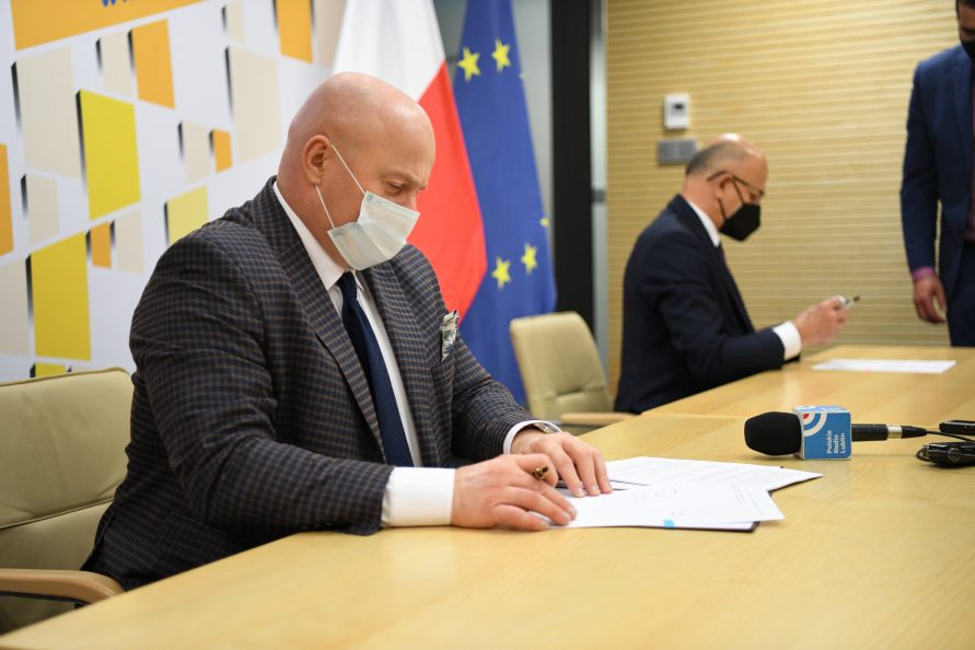 Zdjęcie przedstawiąjące na pierwszym planie siedzącego przy stole Marszałka Województwa Lubelskiego Jarosława Stawiarskiego, obok niego na dalszym planie również siedzącego Prezydenta Miasta Lublin Krzysztofa Żuka