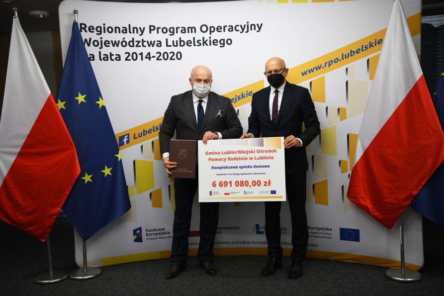 Zdjęcie przedstawiąjące stojących Marszałka Województwa Lubelskiego Jarosława Stawiarskiego i Prezydenta Miasta Lublina Krzysztofa Żuka, trzymających wspólnie symboliczny czek dla Miejskiego Ośrodka Pomocy Rodzinie w Lublinie