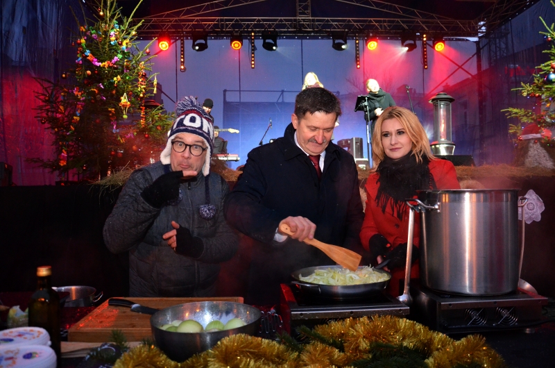 Zdjęcie przedstawiające trzy osoby, dwóch mężczyzn i jedną kobietę, którzy ubrani w zimowe ubrania stoją w kuchni znajdującej się na wolnym powietrzu i gotują w takich warunkach potrawy wigilijne