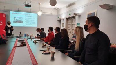 Zdjęcie na którym widnieje sala z uczestnikami spotkania siedzacymi rpzy stole na scianie wyswietlona prezentacja