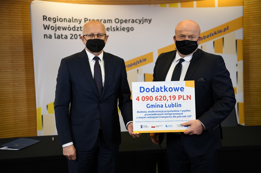 Zdjęcie przedstawia dwóch stojących mężczyzn, jeden z nich to marszałek województwa Lubelskiego Jarosław Stawiarski a drugi to prezydent miasta Lublin Krzysztof Żuk. Obaj trzymają w rękach symboliczny czek na projekt rozwoju systemu komunikacji miejskiej