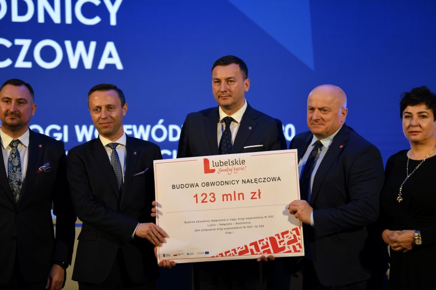 Zdjęcie przedstawiające 4 mężczyzn i jedną kobiete, którzy są rezprezentantami władz wojewodztwa oraz firmy Strabag. wszystkie osoby stoją i wspólni trzymają symboliczny czek z wypisaną kwotą na budowę obwodnicy Nałęczowa