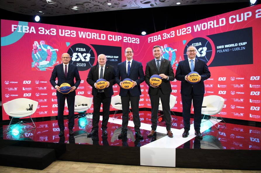 Grupa pięciu mężczyzn stojących w rzędzie do zdjęcia, na scenie, za nimi stoi duży telebim wyświetlający napis: Fiba 3x3 U23 World Cup 2023