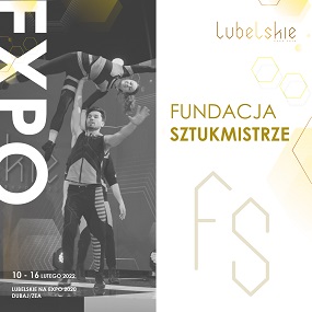 Zdjęcie przedstawia dówch akrobatów kobietę i mężczynże w trakcie wykonywania sztuczki cyrkowej podczas której męzcyzna trzyma kobietę na rekąch uniesioną w góre w tle napis Fundacja Sztukmistrze