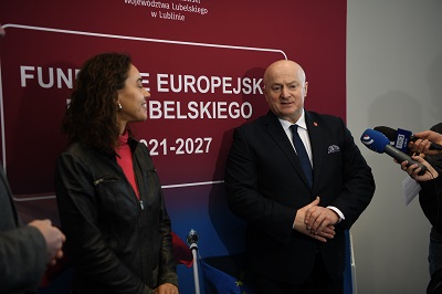 Zdjęcie przedstawiające kobietę i mężczynzę którzy stoją obok siebie i udzielają wypowiedzi do stojącego mikrofonu