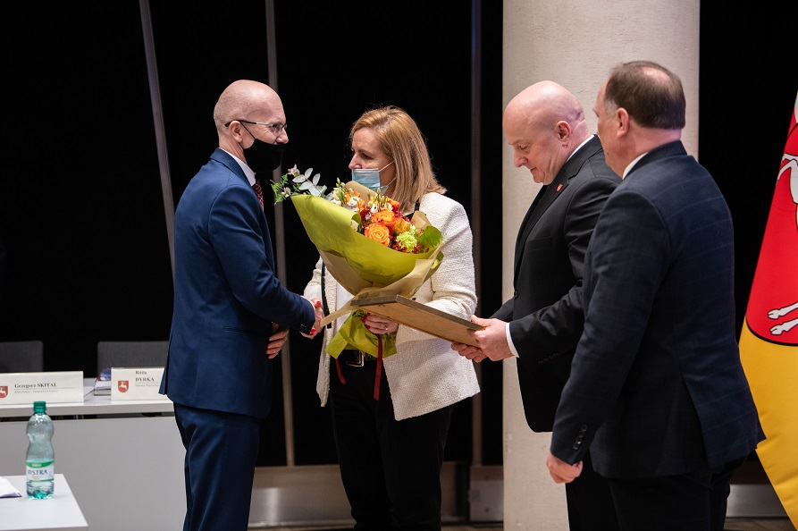 Zdjęcie przedstawia trzech mezczyzn i kobiete. kobieta wręcza jednemu z męzczyzn kwiaty.