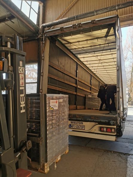 Palety z zapakowanymi darami i mężcyzna pakujący je do wnętrza otwartego tira.