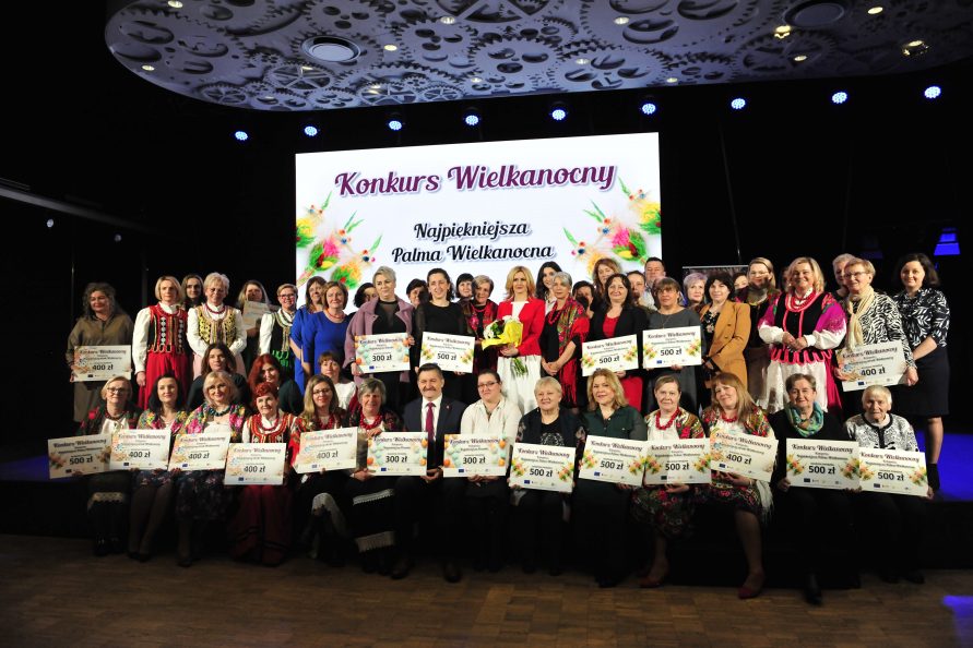 Grupa kobiet pozująca do zdjęcia. Kobiety ustawione są w dwóch rzędach, znajdują się w sali konferencyjnej i trzymają w rękach dyplomy. Są laureatkami konkursu.