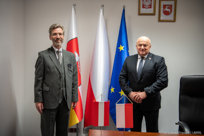 Dwóch mężczyzn stoi na tle ustawionych za nimi flag