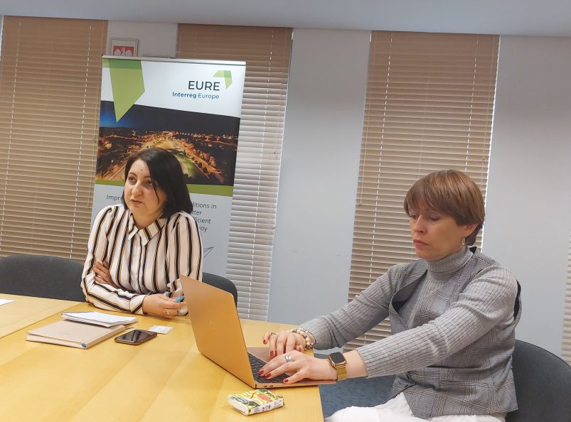 dwóch prelegentów spotkania za stołem w tle roll-up projektu