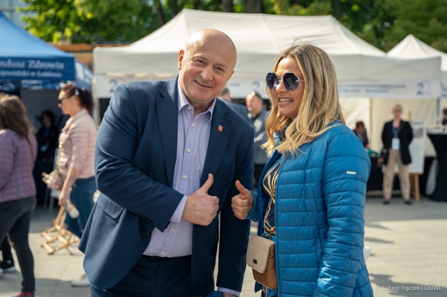 Zdjęcie przedstawia sześć osób różnej płci siedziących przy stole. Dwie osoby na miejscach pośrodku stołu stoją. Jedna z nich trzyma kartkę a przed drugą z nich stoi puchar.