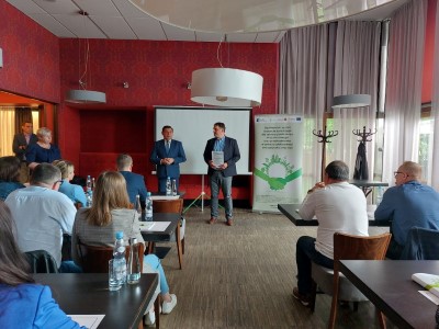 Pan Janusz Bodziacki - Dyrektor Departamentu Środowiska i Zasobów Naturalnych przemawia do uczestników szkoleń przed wręczeniem zaświadczeń. Uczestnicy szkoleń siedzą w ławkach. Obok dyrektora stoi troje Doradców Energetycznych. W tle stoi baner projektu Doradztwa Energetycznego.