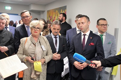 Widok na korytarz na którym stoi duża liczba osób, na pierwszym planie znajduje się jedna kobieta i dwóch męzczyzn, którzy stoja przed wyciągniętymi mikrofonami