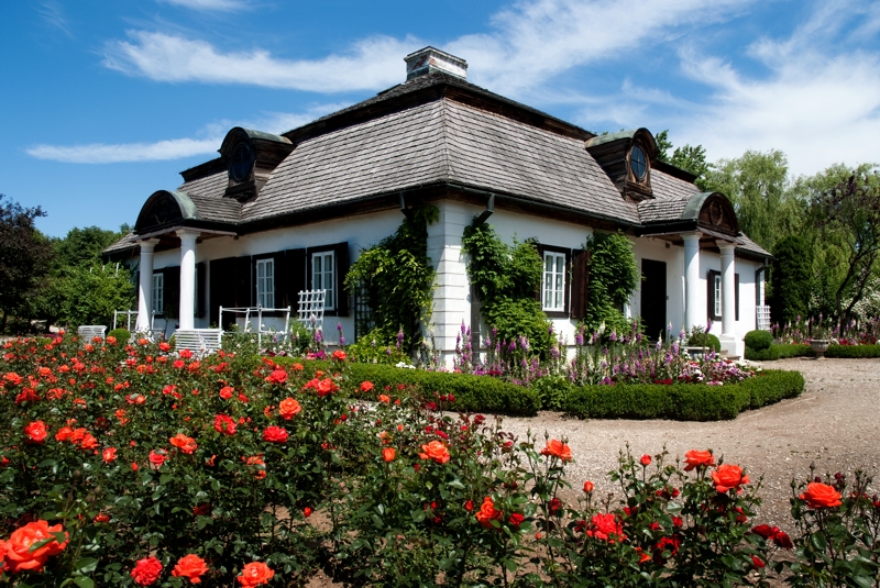 Widok na budynek dworku szlacheckiego, przed nim ogród z kwitnącymi kwiatami