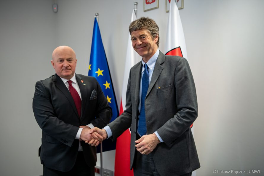 Dwóch mężczyzn podających sobie rękę na tle flagi Polskiej i Europejskiej