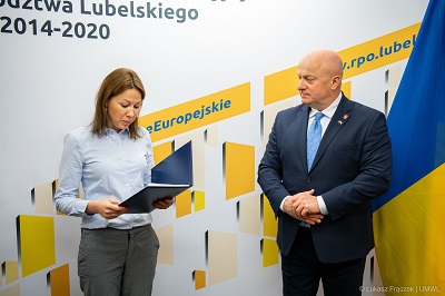 Kobieta i mężczyzna stoją obok siebie, kobieta trzyma w rekach otwartą teczką z dokumentami