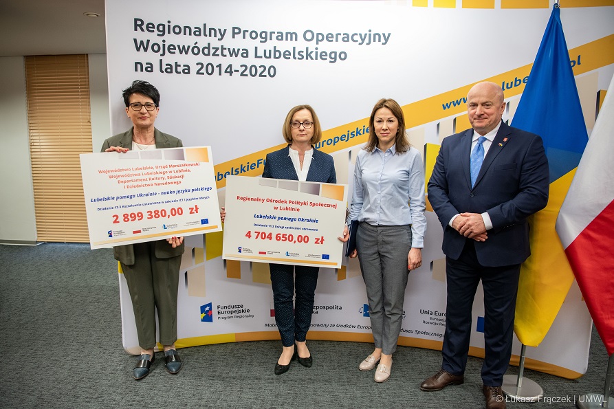 Trzy kobiety i meżczyzna stoją obok siebie. Dwie z kobiet trzymają w rękach symboliczne karty z informacją o wysokosci dofinansowania