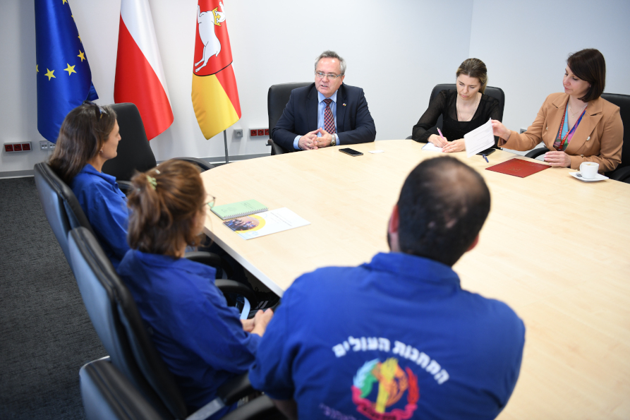 Grupa osób kobiet i mężczyzn siedzących przy stole w pomieszczeniu w trakcie rozmowy.