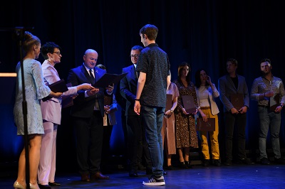 Grupa młodzieży stoi na scenie i odbiera od przedstawicieli Urzędu Marszałkowskiego dyplomy