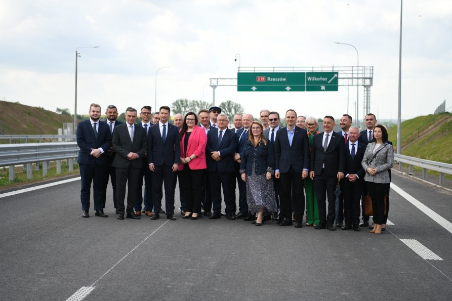 Uczestnicy wydarzenia w grupie na tle ulicy oraz drogowskazu (zdjęcie grupowe)